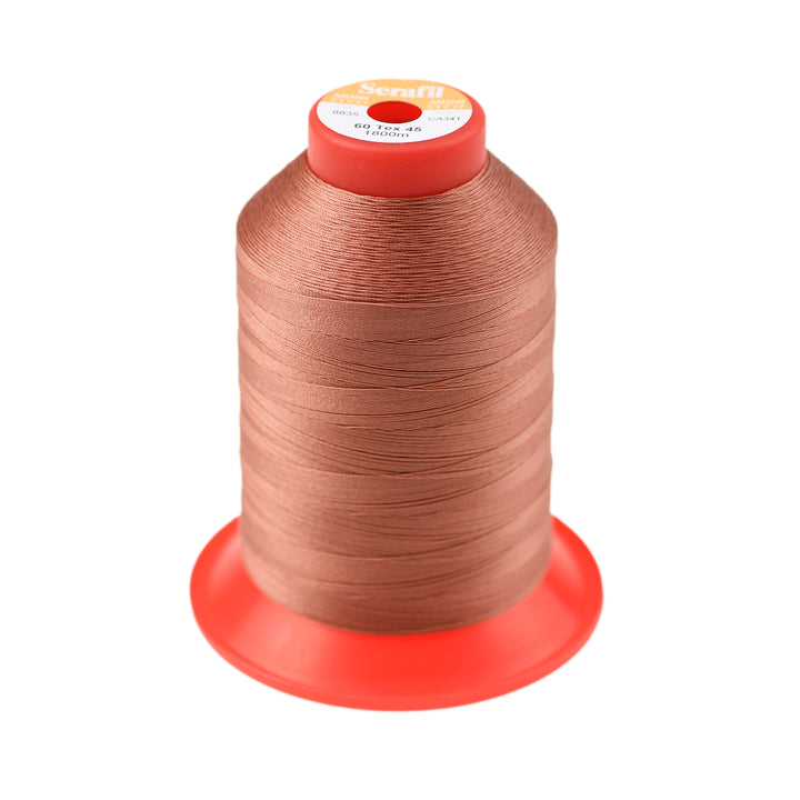 Spool of light rust coloured thread on a red plastic stand with a white background