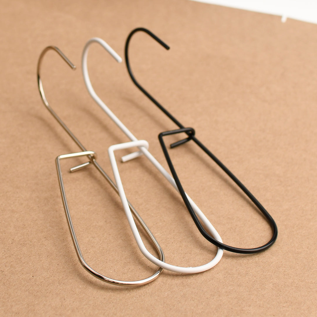 Three metal pattern hooks/ utility hooks in silver, white, and black on a brown background